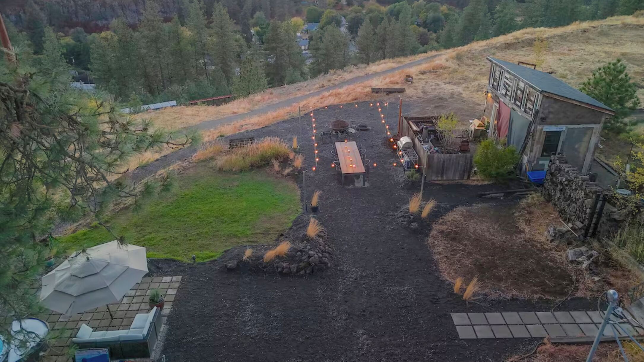 A rustic outdoor setting with a wooden table and chairs, surrounded by a dirt path and a small garden area.