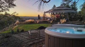 A backyard with a hot tub, a patio with a table and chairs, and a gazebo.