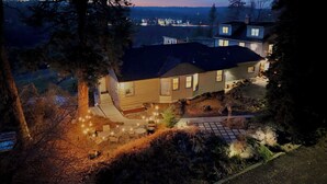 A two-story house with a well-lit patio area, a stone pathway, and a view of the surrounding landscape. - Garden Bodega on Sunset Ridge, Near Downtown, Hot tub, all with Panoramic View (Spokane)