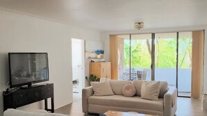 A modern living room with a sofa, a coffee table, a TV on a stand, and a sliding glass door leading to an outdoor area. - Beautiful, Large Bondi Room with Private Ensuite (Bondi Junction)
