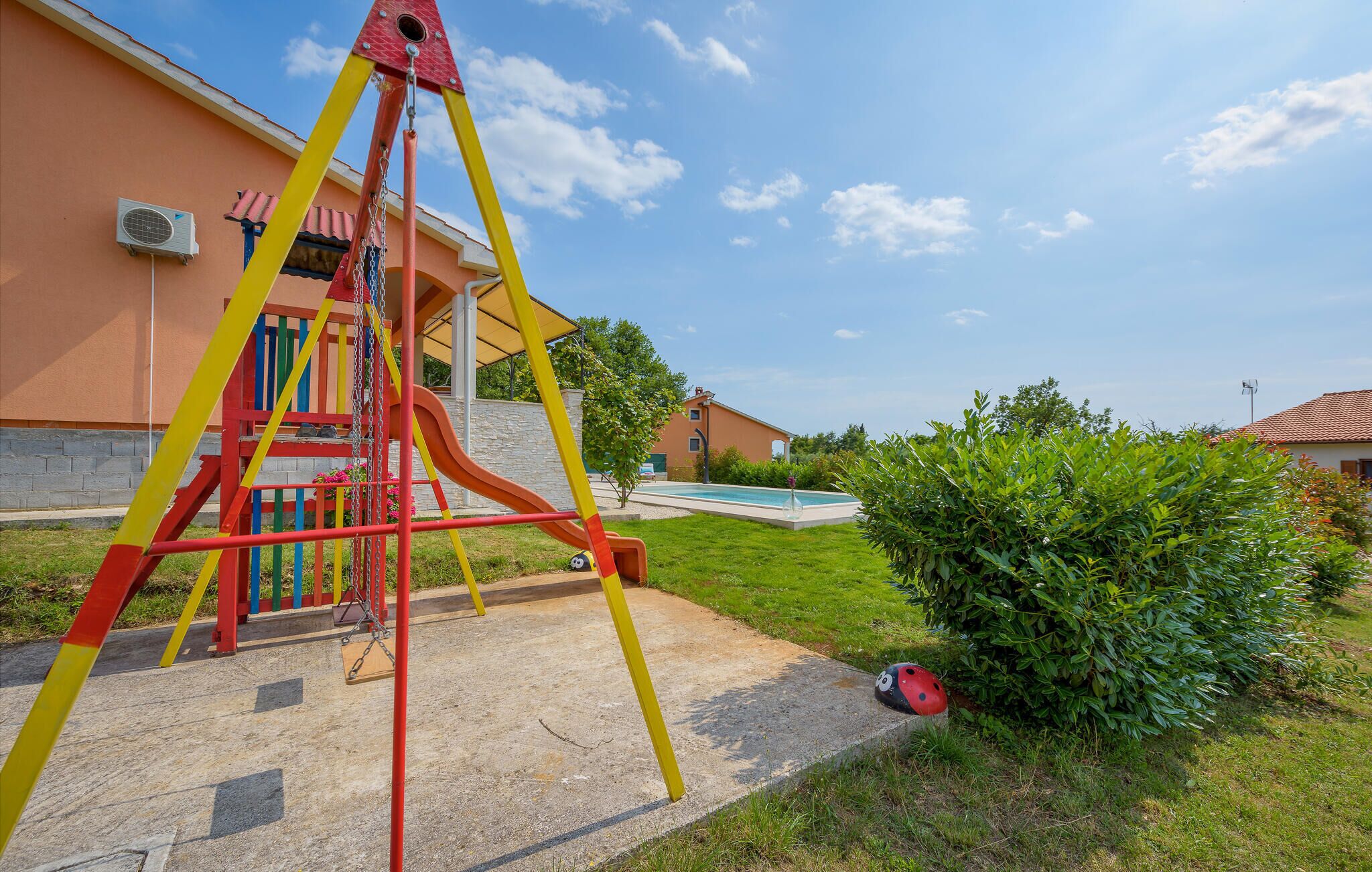 A playground with a slide and swings, a swimming pool, and a house in the background.