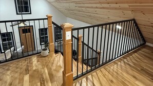 Un loft spacieux avec un plafond en bois, une rambarde noire et une vue sur le niveau inférieur.