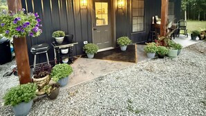 Une maison en bois sombre, dotée d’un porche, de plantes en pot et d’une allée gravillonnée.