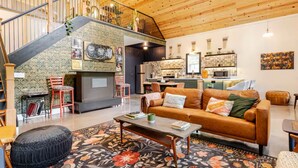 Un vaste espace de vie doté d’un plafond en bois, d’un escalier, d’une cuisine et d’un coin salon confortable avec un canapé et un pouf.
