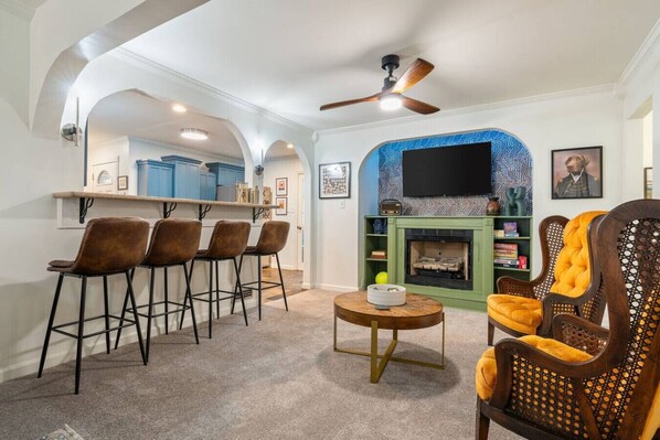 A living room with a fireplace, a television, and a bar area with stools.