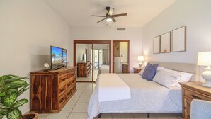 Une chambre à coucher comprenant un lit, une commode en bois, un téléviseur et un ventilateur de plafond.