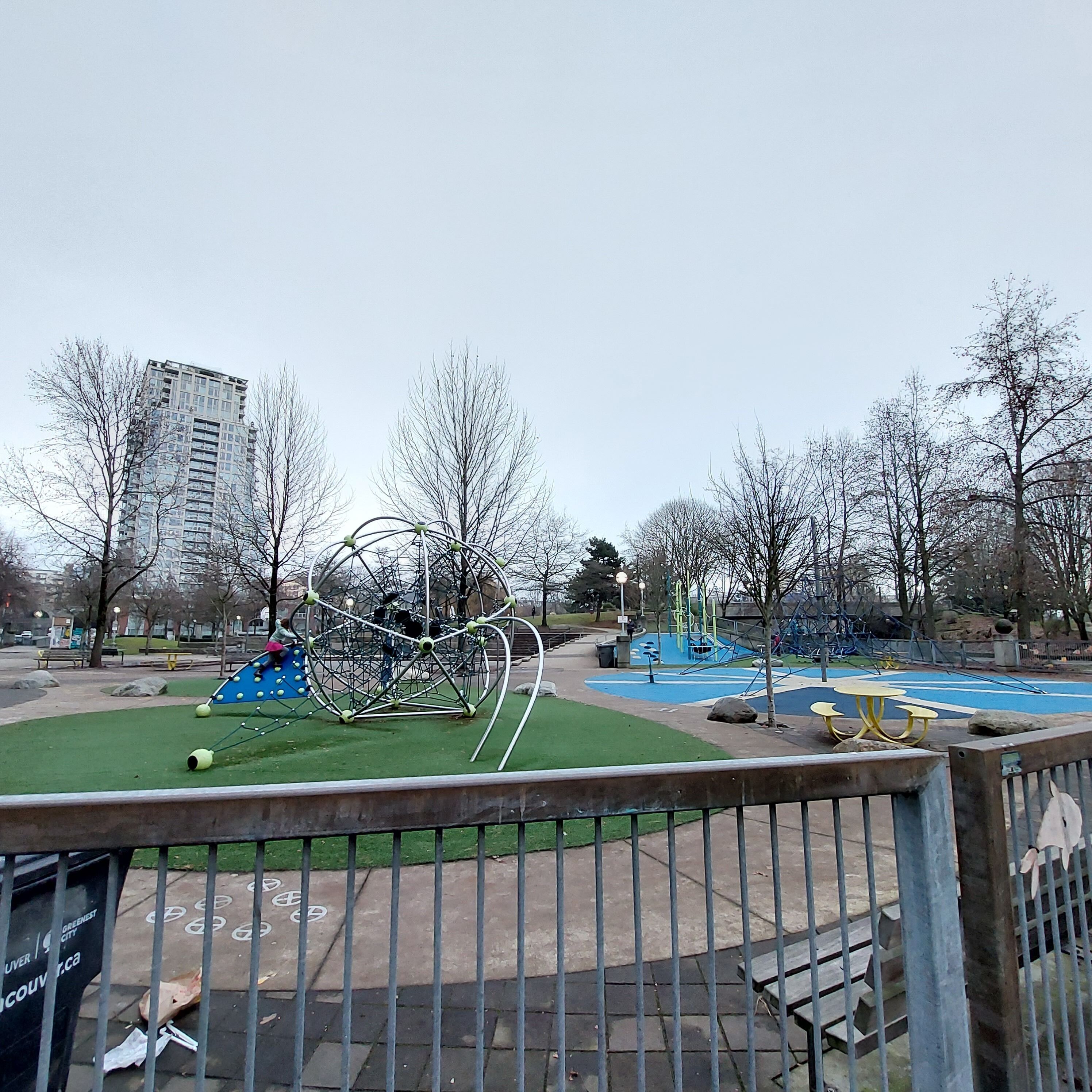 Un parque infantil con una estructura circular para escalar, una casita azul y una mesa amarilla.