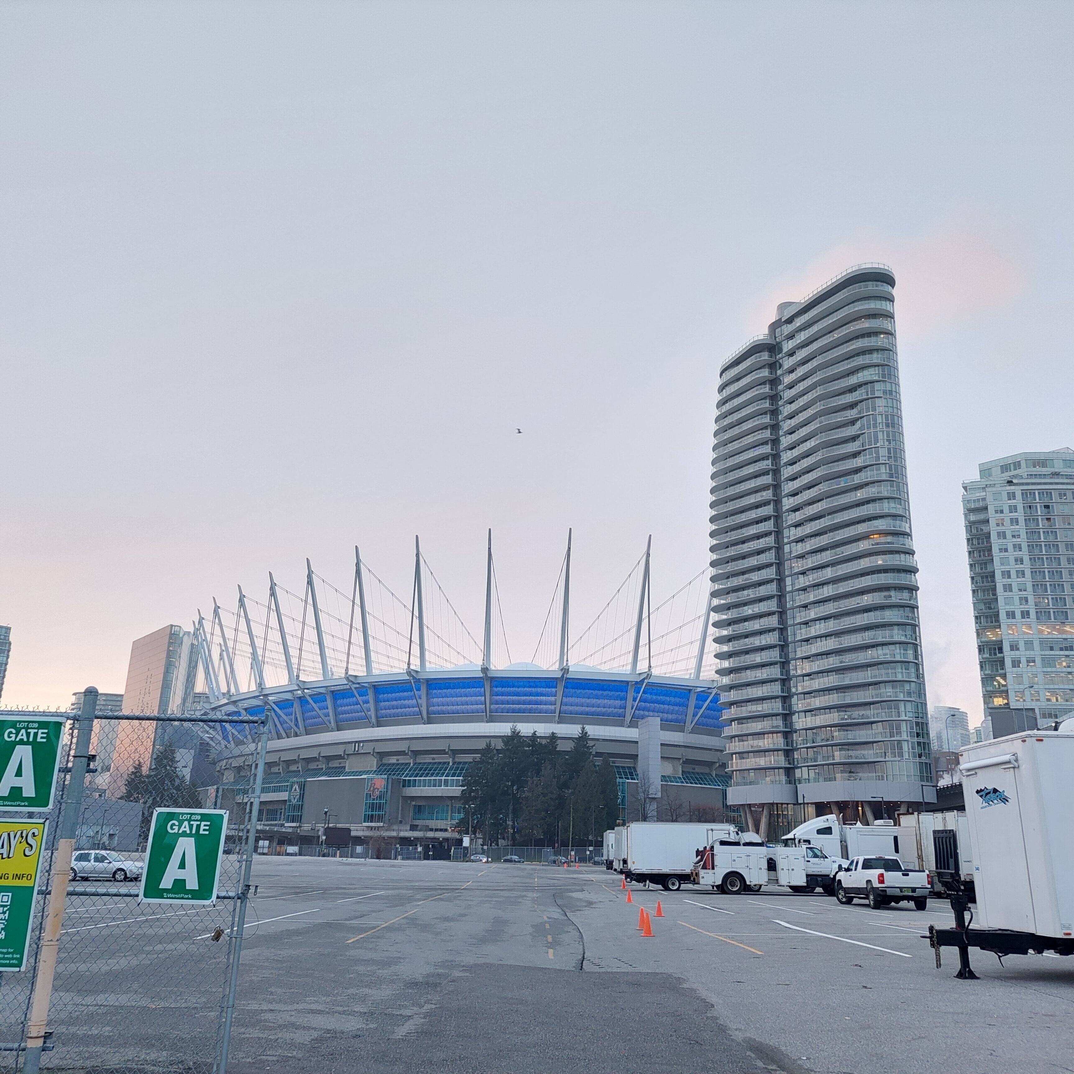 A parking lot with a large stadium in the background, surrounded by tall buildings.