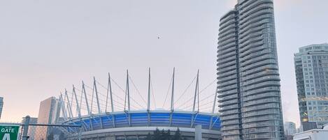 A parking lot with a large stadium in the background, surrounded by tall buildings.
