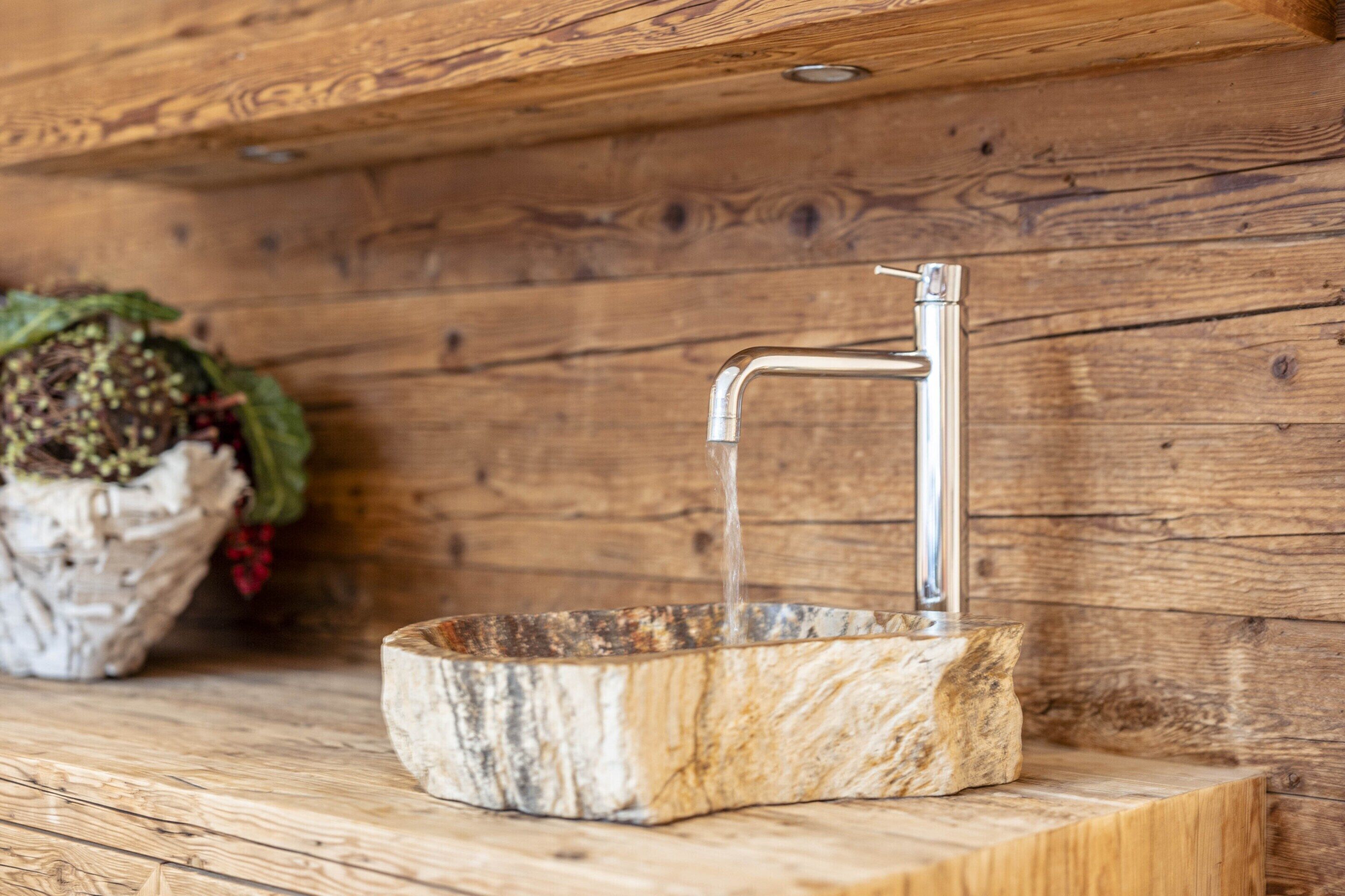 A rustic wooden wall with a metal faucet and a basin.