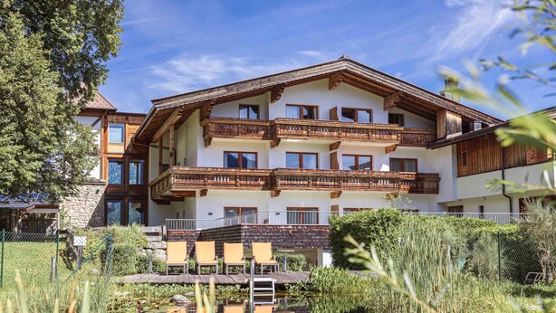A multi-story hotel with balconies, a pond, and surrounding greenery. - Nice Apartment With Balcony (Reith bei Kitzbuehel)