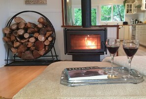 A cozy room with a wood-burning stove, a pile of firewood, and two glasses of red wine on a tray. - Idyllic Farm Stay at Wolka Park in Bilpin! (Bilpin)
