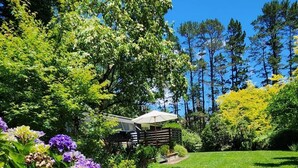 Un jardin luxuriant, parsemé de fleurs violettes, avec un sentier menant à un bâtiment doté d’un espace de repos abrité.