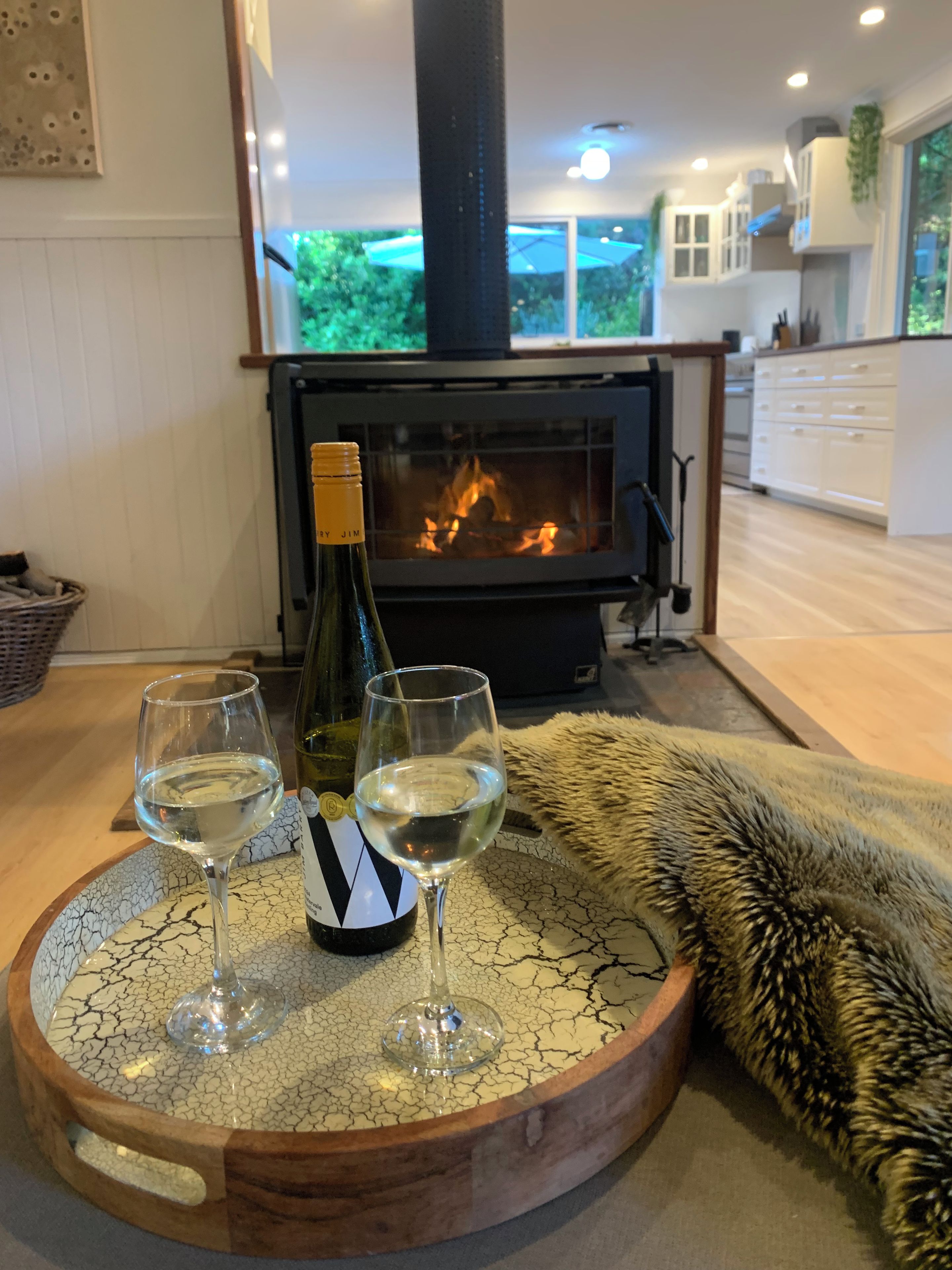 Une pièce chaleureuse avec une cheminée, une bouteille de vin et deux verres posés sur un plateau en bois rond.