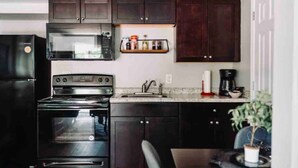 Une cuisine avec des meubles de couleur sombre, un four à micro-ondes, une cuisinière, un évier et une étagère remplie de bocaux.