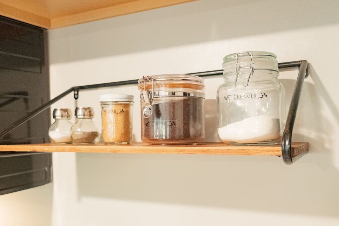 A shelf with various glass containers, including a jar labeled 'CREAMER' and a metal pitcher.