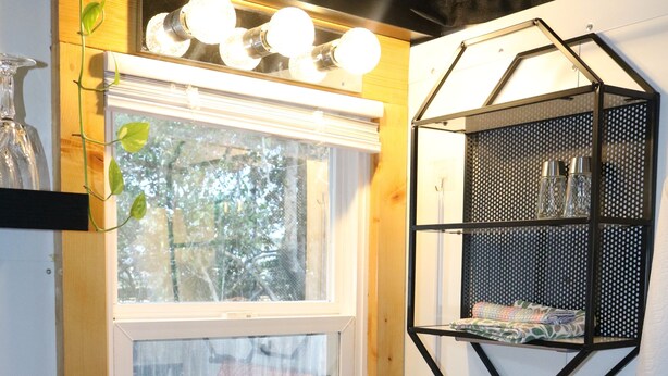 A kitchen with a wooden countertop, a stainless steel sink, a window with a view, a hanging pot rack, and a black metal shelf with glassware. - Charming Backyard Studio/Tiny Home in beautiful Jacksonville/OP  (Jacksonville)