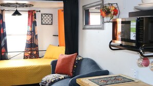 A compact room with a bed, a sofa, a microwave, and a small table with a decorative item. - Charming Backyard Studio/Tiny Home in beautiful Jacksonville/OP  (Jacksonville)