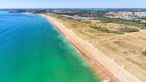 An aerial view of a coastal area with a sandy beach and a clear blue sea.