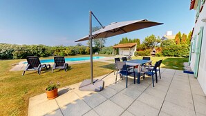 A patio with a table and chairs, a pool, and a lawn.