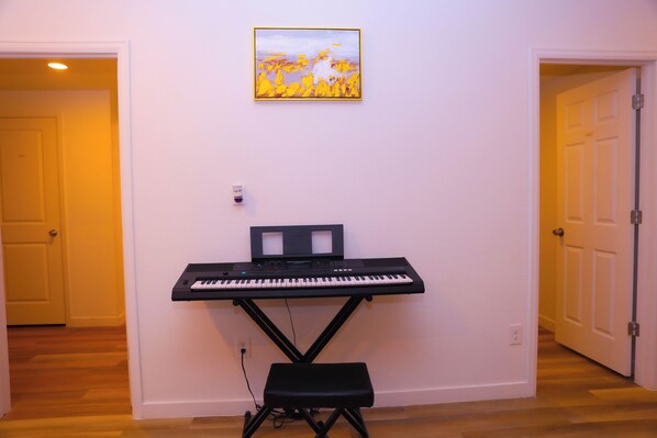Una habitación con un teclado de pie y un banco, un cuadro en la pared y suelo de madera.