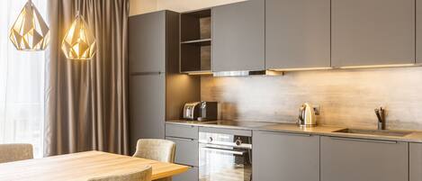 A modern kitchen with grey cabinets, a wooden dining table, and pendant lights.