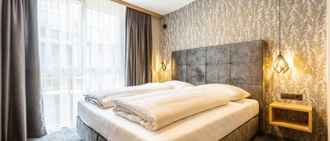 Une chambre d’hôtel moderne avec un grand lit, une tête de lit, deux lampes de chevet et une fenêtre avec des rideaux.