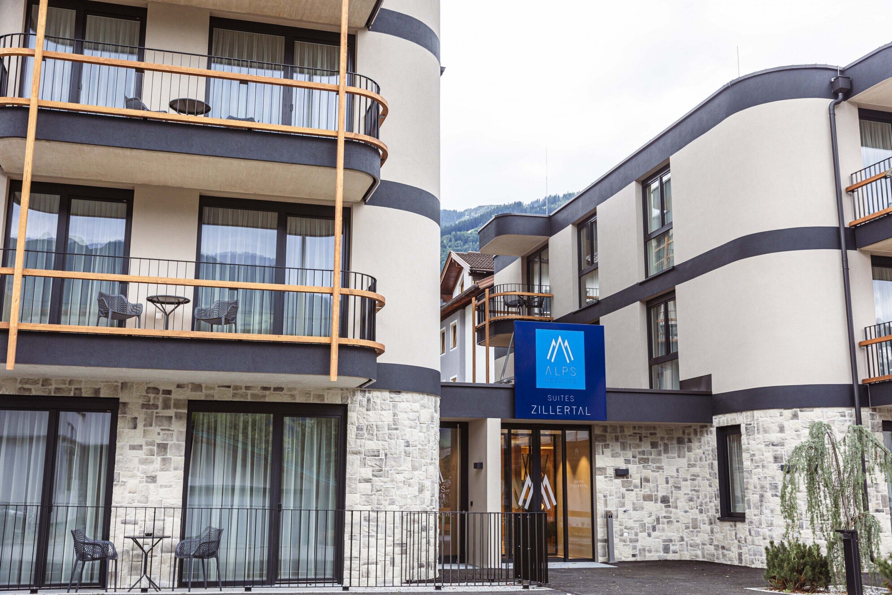 Un hotel con fachada de piedra, balcones con mobiliario exterior y un cartel que dice 'ALPS Suites Zillertal'.