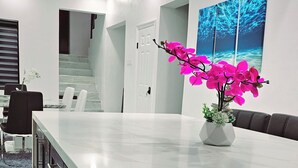 Una cocina moderna con encimera de mármol, una isla central con taburetes de bar, una lámpara de araña de cristal colgante y una planta de orquídea vibrante.