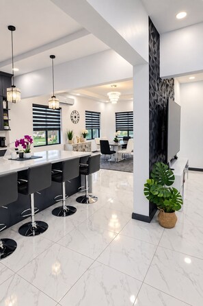 A modern kitchen with a central island, bar stools, pendant lighting, and a view of the outdoors.