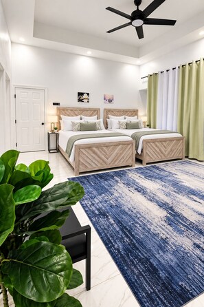 A bedroom with two beds, a ceiling fan, a large blue and white patterned rug, and a green plant. - Modern Oceanview Villa. All Bedrooms with Private Bathrooms. Private Pool (St. Ann Parish)