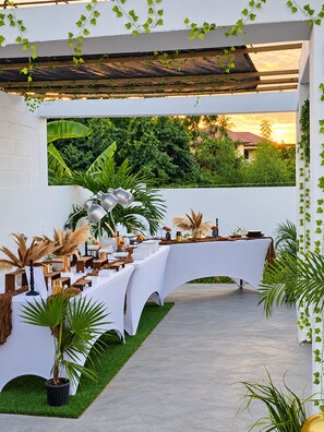Un espace de restauration en plein air avec une table blanche, placée devant un décor de verdure et offrant une vue sur le coucher de soleil.