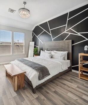 A modern bedroom with a geometric wall design, a wooden headboard, a large bed with white bedding, a bench, and a wooden nightstand. - 5 Minutes to Downtown + GARAGE! Near George R Brown Convention/Med Center/NRG (Houston)