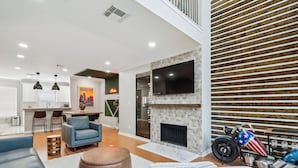 A modern living room with a fireplace, a motorcycle, and a kitchen area in the background. - 5 Minutes to Downtown + GARAGE! Near Med Center/NRG/George R Brown Convention (Houston)