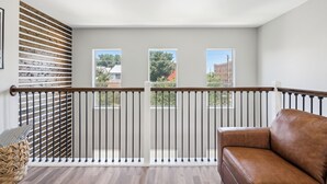 A balcony with a wooden slat wall, a brown leather sofa, and three windows offering views of buildings and trees. - 5 Minutes to Downtown + GARAGE! Near Med Center/NRG/George R Brown Convention (Houston)