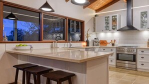 A modern kitchen with a large island, wooden beams, pendant lighting, and a view through the windows. - 'Linden Rise'  cosy farmhouse, peace & charm with views  for miles. (Pakenham Upper)