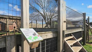 A wooden fence with a metal gate, a wooden staircase, and a sign with a map and text. - Pretty Cabin in Camping Resort (Lokken)