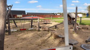 A playground with swings, a slide, and a red bench. - Pretty Cabin in Camping Resort (Lokken)