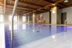 A swimming pool with a wooden ceiling and walls, a few lounge chairs, and a large abstract painting on the wall.