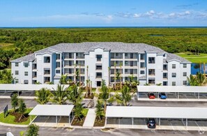 Stunning hotel with a central entrance and balconies on each floor, set amidst lush greenery and a serene body of water.
