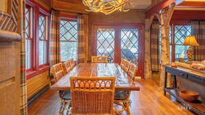 Une salle à manger en bois avec une grande table et des chaises, un lustre et des rideaux à carreaux.