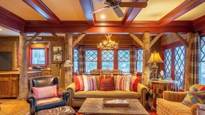 L’intérieur d’une cabane en rondins, avec un plafond en bois, un lustre, un ensemble de canapés et une cheminée.