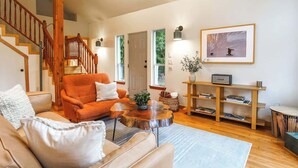 A living room with a staircase, a sofa, a coffee table, and a bookshelf. - Cozy Mt. Baker Escape • Fireplace • Pets (Glacier)
