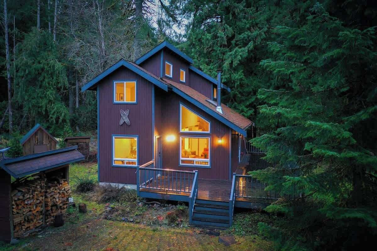 Eine zweistöckige Holzhütte mit steiler Dachneigung, großen Fenstern und einer Holzterrasse.