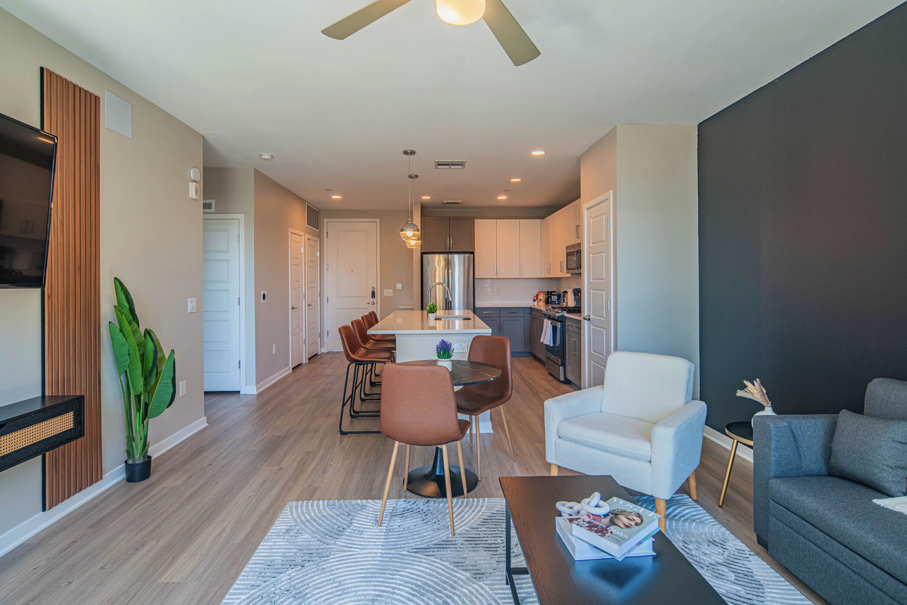A modern living room with a dining area, kitchen, and a ceiling fan.