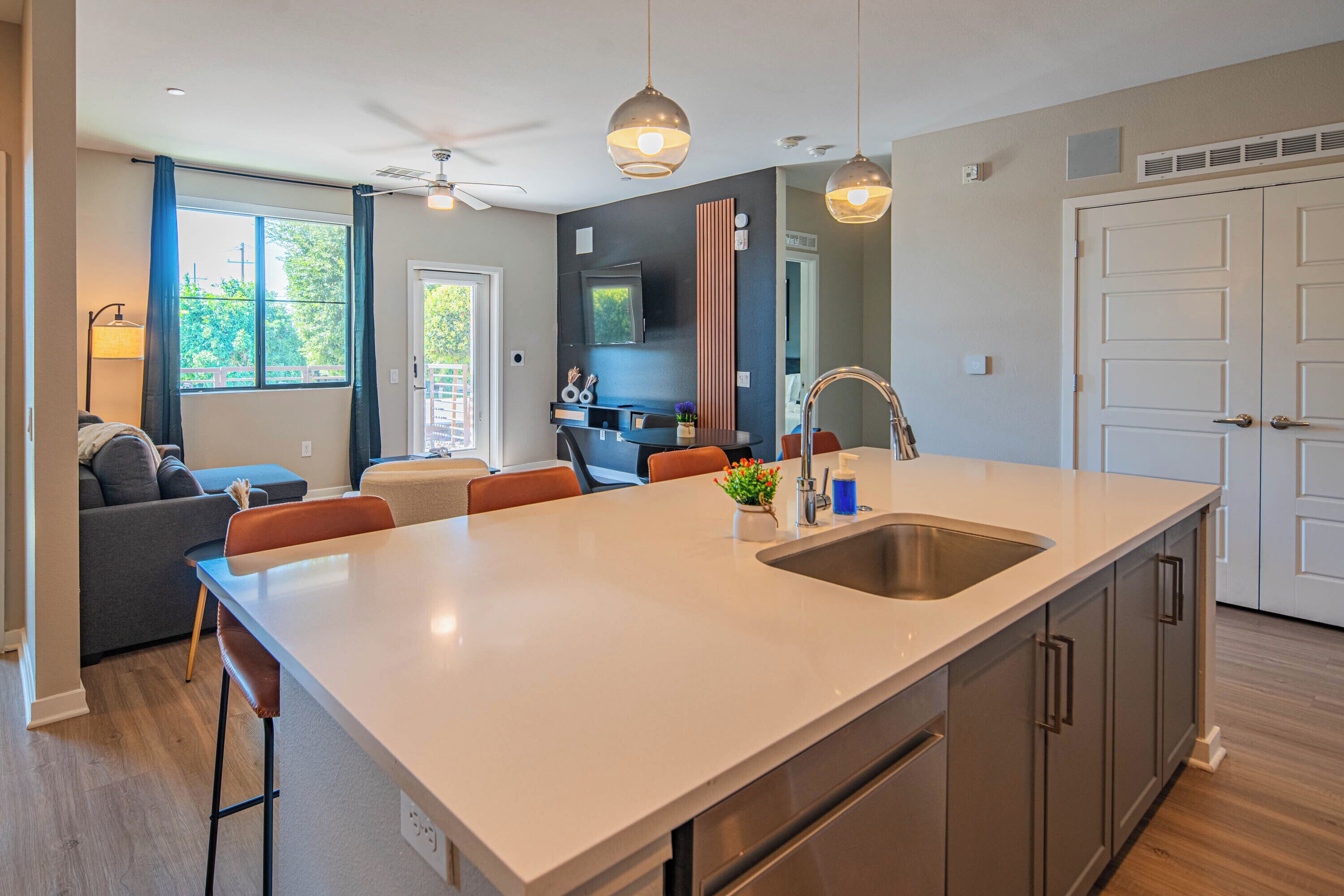 A modern kitchen with a large island, a dining area with chairs, a sofa, and a ceiling fan.
