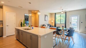 A modern kitchen with a central island, dining area with chairs, and a living room with a sofa. - ROVE LIVING/KL - Alta North Central (Phoenix)