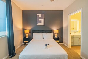 Ein Hotelzimmer mit einem großen Bett, zwei Nachttischen mit Lampen, einem Wandbild und Blick ins Badezimmer.