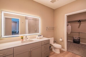 Ein modernes Badezimmer mit einem großen Spiegel, einem Waschbecken, einer Toilette und einem begehbaren Kleiderschrank.