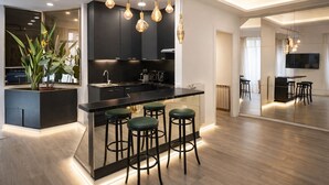 A modern kitchen with a central island, bar stools, pendant lighting, and a large mirror reflecting the space.